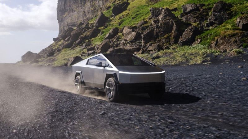 A futuristic looking silver Tesla cybertruck speeds along a rugged, rocky path with green moss and towering cliffs, emitting dust and conveying a sense of power and adventure.
