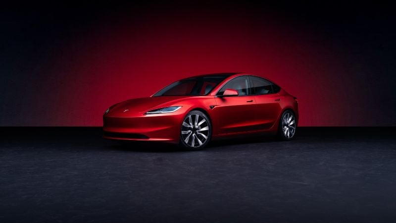A red Tesla Model 3 parked against a dark, gradient background, highlighting its modern design and elegance.