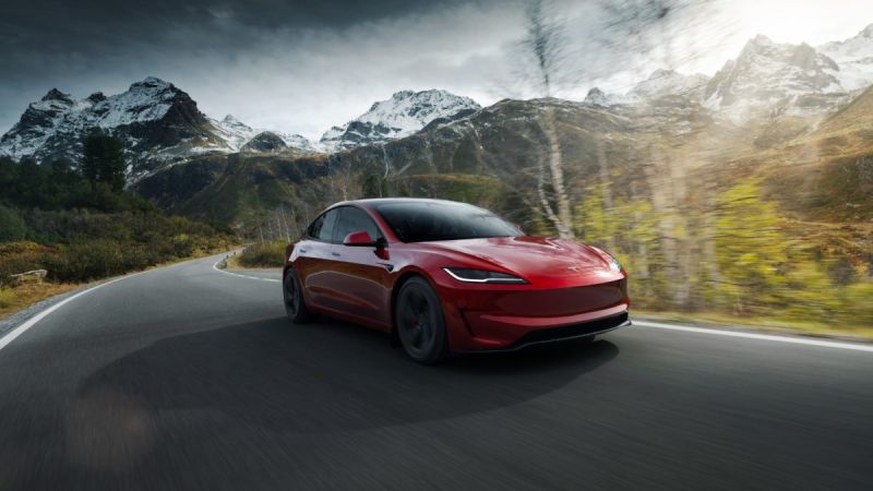 Red Tesla Model S driving on mountain road with snow-capped peaks in background