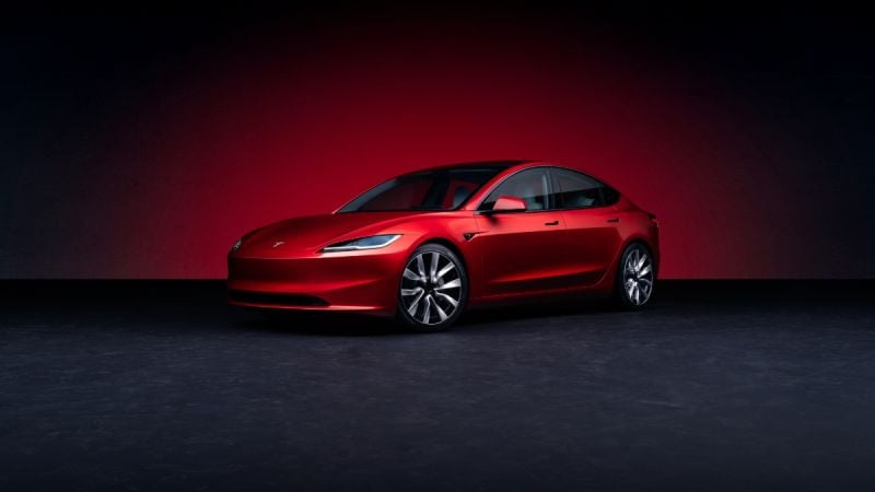 Candy red Tesla Model 3 sedan shown in three-quarter front view against dark background, featuring sleek aerodynamic design and signature LED headlights.