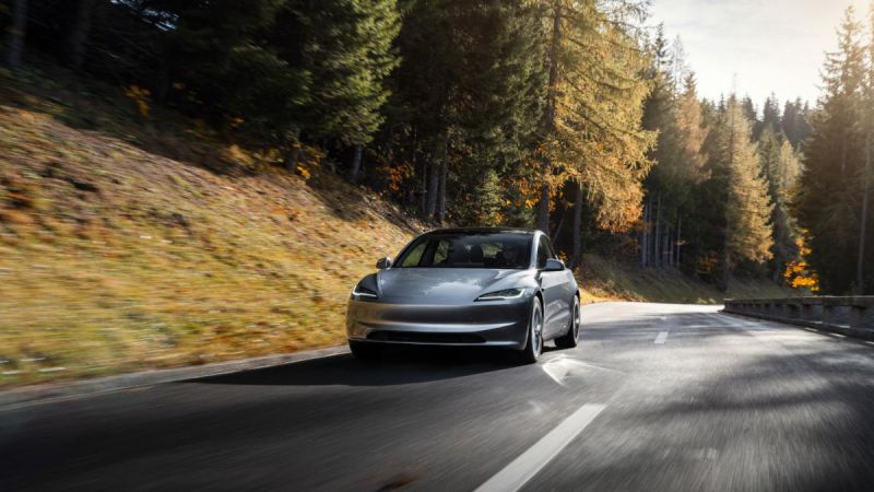 Silver Tesla Model 3 driving on winding forest road during autumn sunset