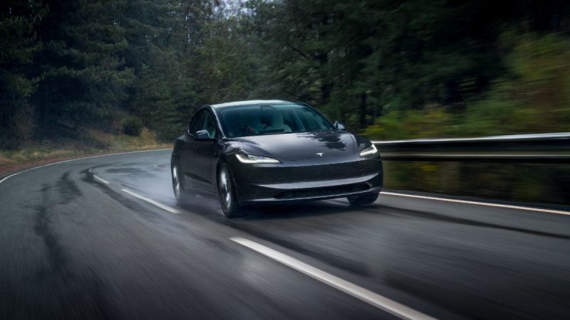 Black Tesla Model 3 navigating a wet, curved forest road with blurred motion and dynamic driving stance