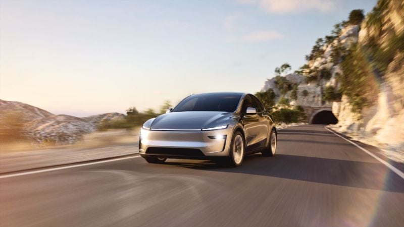 2025 Tesla Model Y electric SUV driving through desert landscape, front three-quarter angle under clear sky.