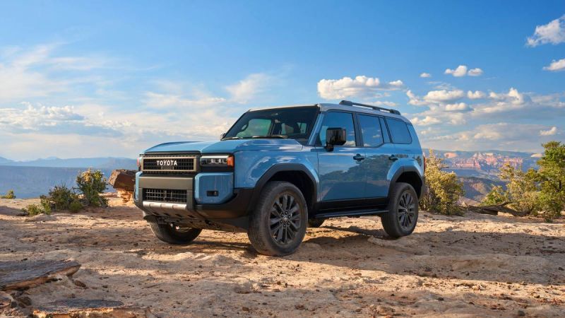 2025 Toyota Land Cruiser 250 Series in blue parked on rocky desert terrain, front three-quarter view highlighting off-road design.
