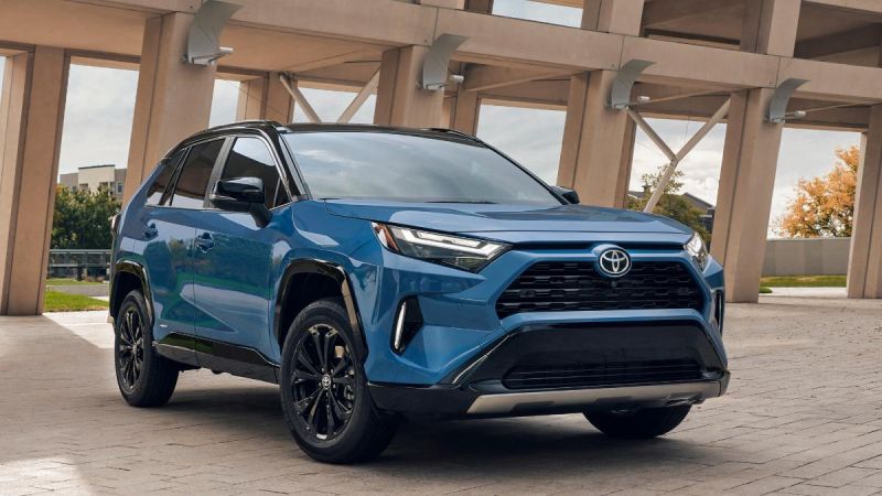 2025 Toyota RAV4 Prime in metallic blue, front three-quarter view, featuring black wheels and aggressive front fascia, parked under modern architectural columns.