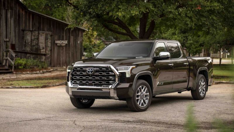 2023 Toyota Tundra Limited in dark brown, front three-quarter view, featuring chrome honeycomb grille and LED headlights, parked near rustic pottery barn.