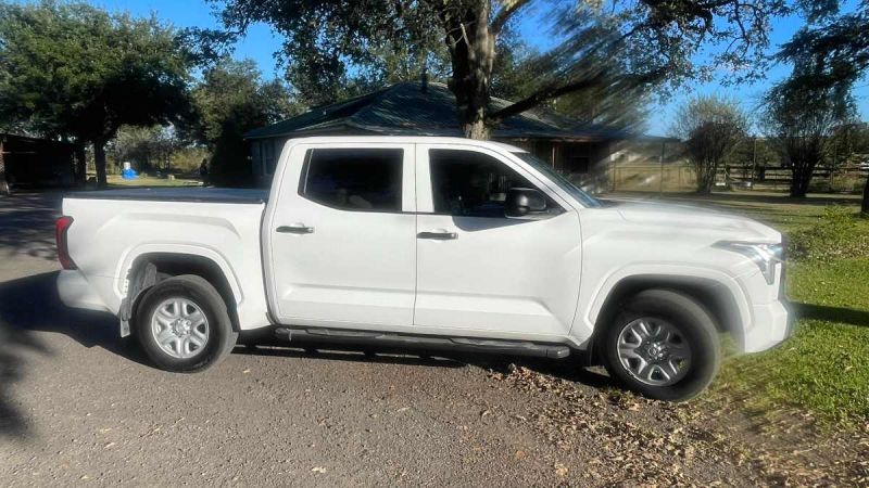 2025 Toyota Tundra crew cab pickup in white, photographed from passenger side, featuring chrome wheels and running boards, parked outside residential home.
