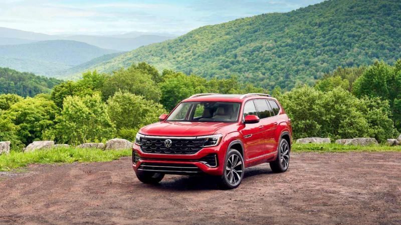 Red SUV parked on a dirt road with lush green hills in the background.