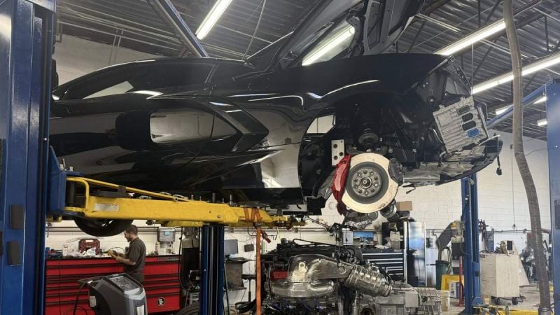 Chevrolet Corvette C8 on a lift with engine removed for repair inside an automotive service workshop.
