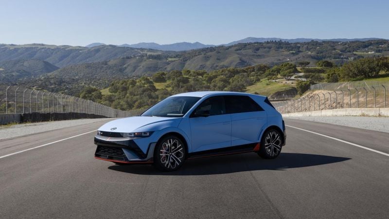 2025 Hyundai IONIQ 5 N in Performance Blue Matte on racetrack, front three-quarter view with mountains and green hills in background