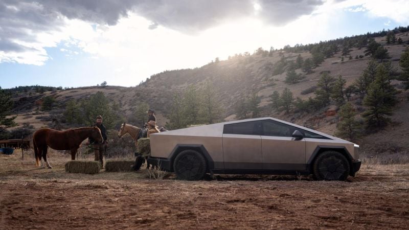 Tesla Cybertruck parked on a rural ranch beside horses and hay bales in a mountainous landscape.