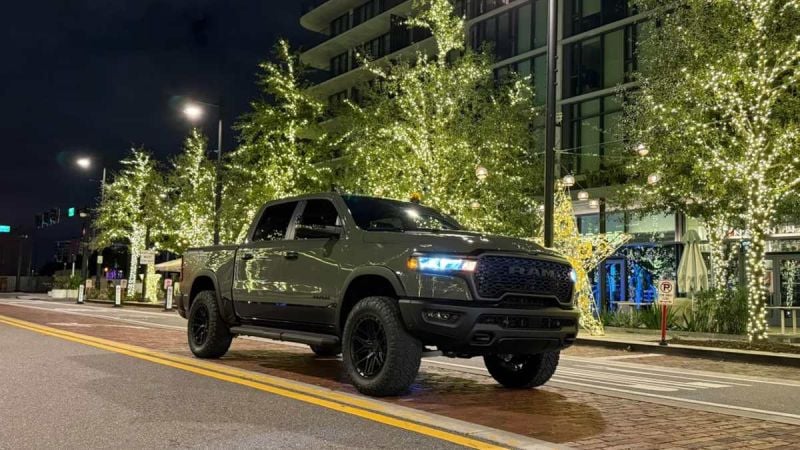 2026 Dodge Ram pickup truck in matte green parked on illuminated city street at night with modern buildings and decorative lights