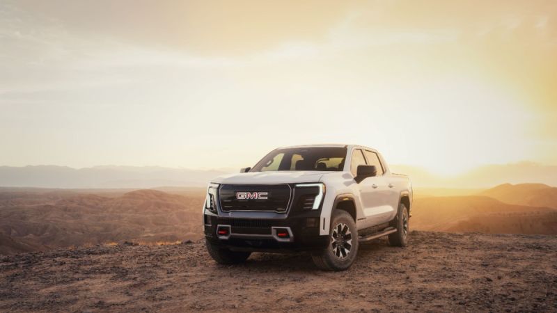 White GMC truck parked on rocky terrain at sunset, with mountains in the background.