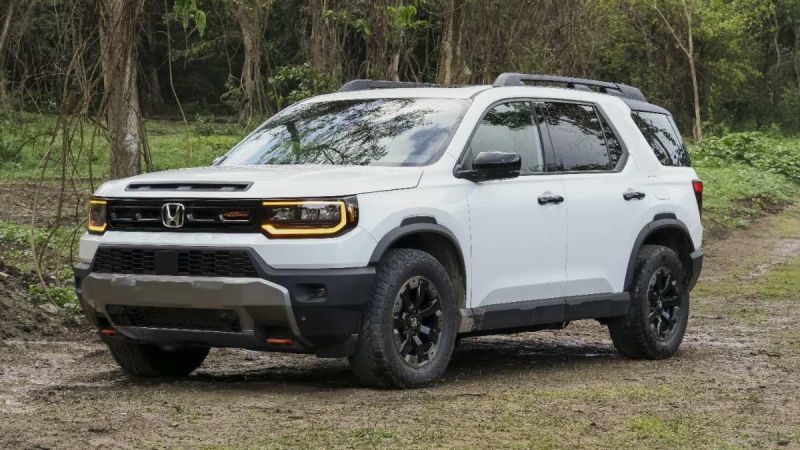White Honda Passport TrailSport SUV parked on muddy forest trail with rugged black wheels and off-road styling