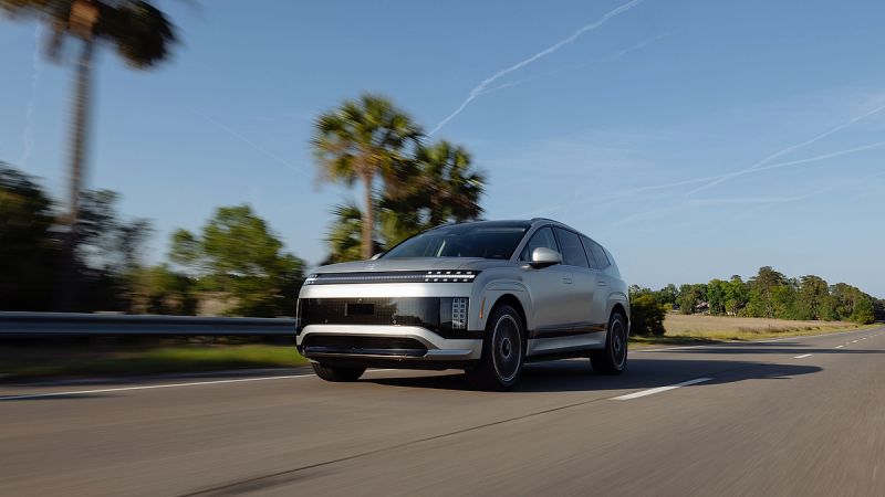 Silver 2026 Hyundai Ioniq 9 electric SUV driving on a sunny road, front three-quarter view