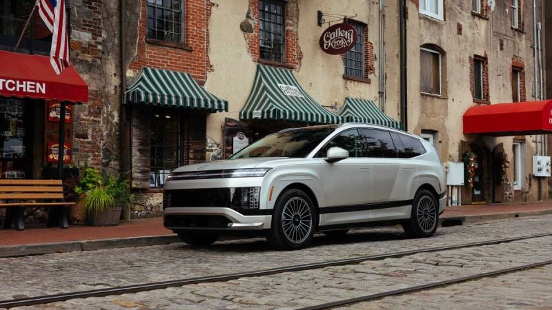 A sleek silver electric SUV parked on cobblestone streets, beside charming brick buildings and awning-covered shops.