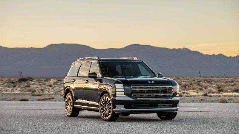 Black 2024 Hyundai Palisade, SUV, front three-quarter view, featuring gold multi-spoke wheels and white racing stripes, photographed in desert landscape at sunset.