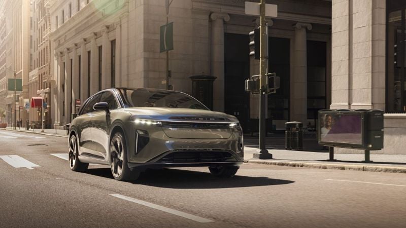 Silver electric SUV driving on urban street with classical architecture and morning sunlight