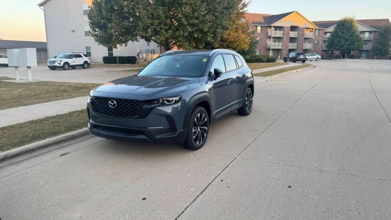 2026 Mazda CX-50, in metallic blue, side profile view, featuring black trim, distinctive two-tone alloy wheels, parked outside dealership.