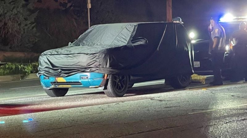 2026 Rivian R2 electric SUV front three-quarter view in colorful camouflage wrap driving on city street at night.