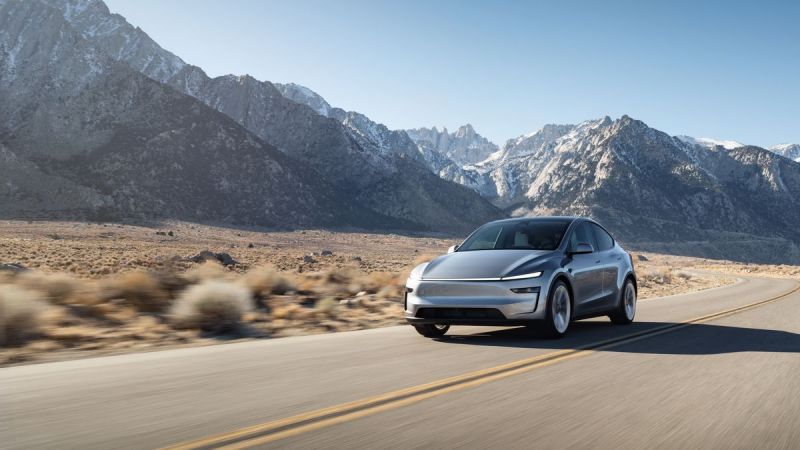 Photograph of a 2026 Tesla Model Y electric SUV in the Juniper color, shown from a three-quarter front angle with the vehicle's front grille, headlights, and side profile clearly visible against a plain background.