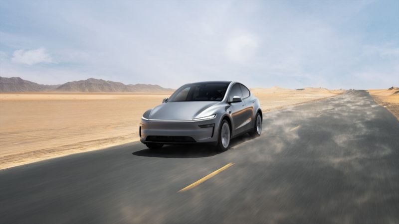 Silver 2026 Tesla Model Y driving on desert road with mountains, dynamic motion blur showing speed and movement