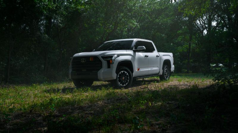 2026 Toyota Tundra in white, photographed at three-quarter front angle in a wooded setting, featuring black accents and distinctive alloy wheels.