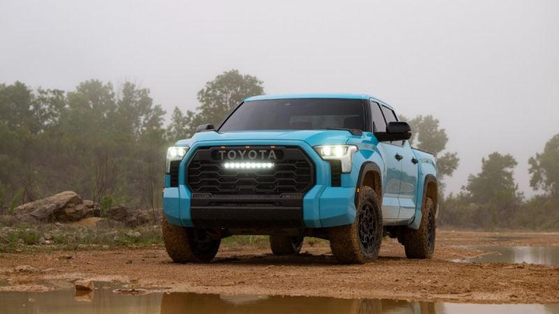 2026 Toyota Tundra TRD Pro in blue driving off-road, front view with LED light bar, aggressive grille, and foggy forest background.