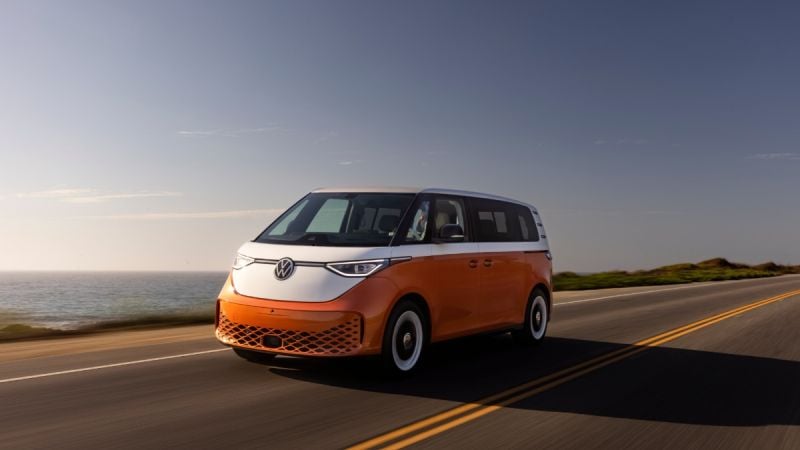 Orange and white Volkswagen ID.Buzz electric van driving on coastal highway at sunset