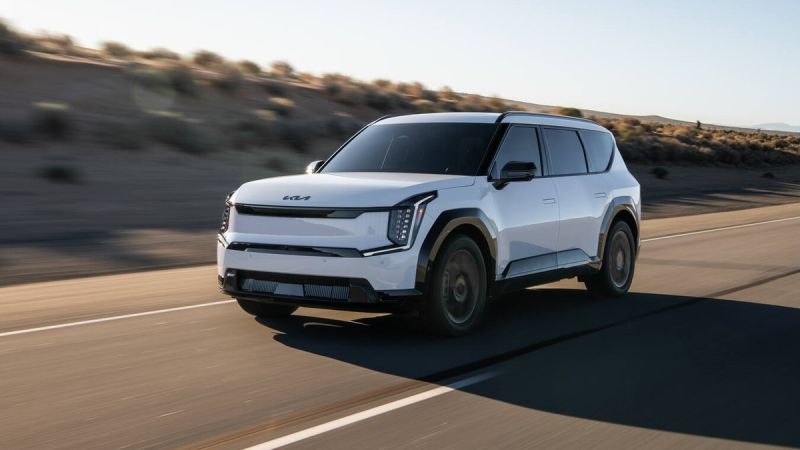 A sleek white Kia electric SUV driving on a desert road, showcasing its modern design and aerodynamic features under a clear sky.