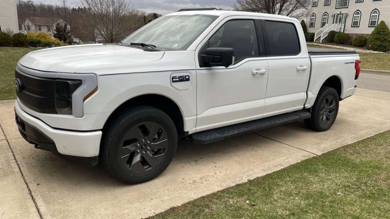 A white Ford F-150 Lightning truck parked on a driveway, showcasing its sleek design and black alloy wheels.
