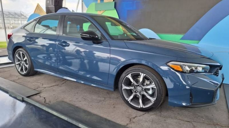 A dark blue 2025 Honda Civic is showcased indoors on a concrete surface. The car features modern design elements and curved lines, conveying a sense of elegance.