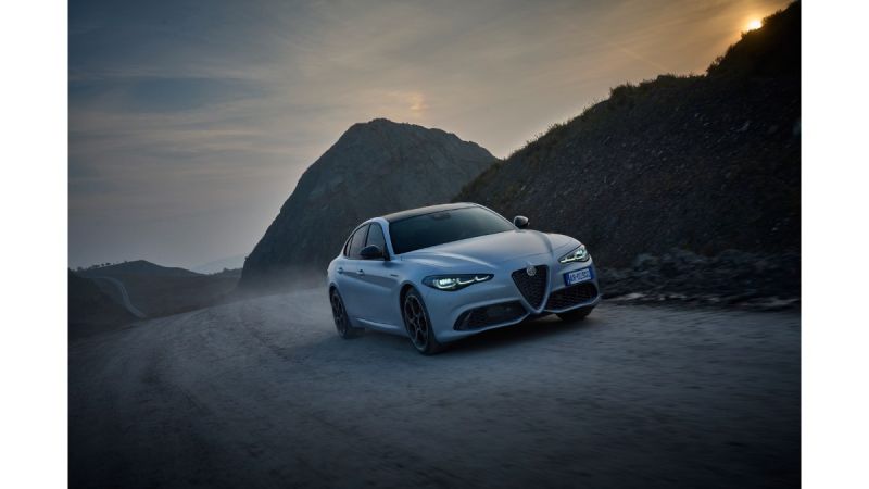 Alfa Romeo driving on misty mountain road at dramatic sunset with rocky landscape