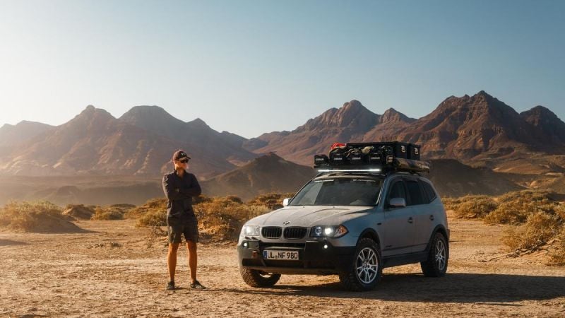 BMW x3 in Desert, person standing next to it with mountains in background