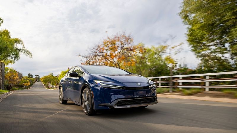 Blue Toyota Prius driving on suburban road with trees and houses