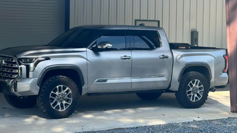Silver 2023 Toyota Tundra with large tires parked under a metal carport. The truck has tinted windows and a modern design, conveying strength and utility.