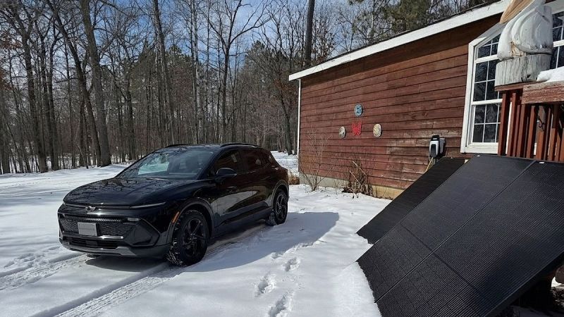 Chevrolet Equinox EV parked outside house connected to portable solar panels in snow