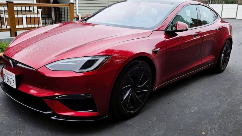 A red Tesla Model S Plaid shown from a front three-quarter angle, featuring its distinctive LED headlights and aggressive front design with black accents and wheels.