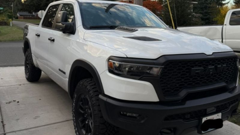 White 2025 Ram 1500 Rebel pickup truck shown featuring its distinctive wide body, hood scoop, and black trim accents.