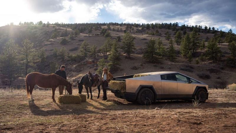 Tesla Cybertruck parked near horses with hay bales in rugged mountain landscape at golden hour