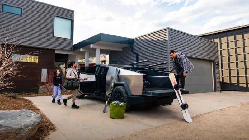 A 2025 Tesla Cybertruck parked in a modern driveway, with three people loading snowboards and gear for an outdoor adventure.