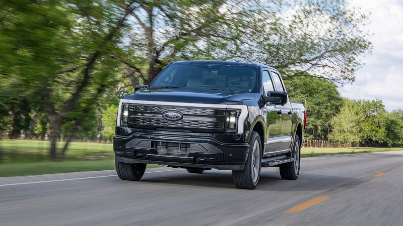 Ford F150 Lightning Platinum electric pickup truck driving on a road through trees