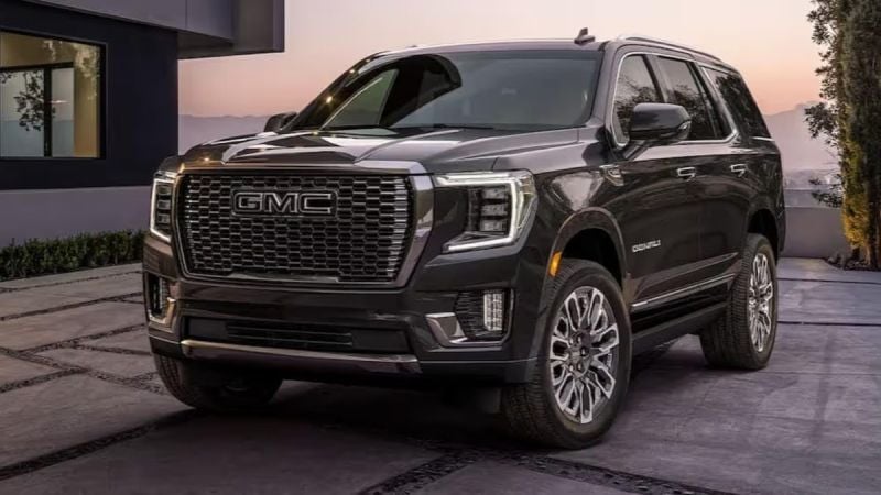 Black and silver 2025 GMC Yukon Denali parked in a desert landscape with rugged terrain and canyon cliffs.