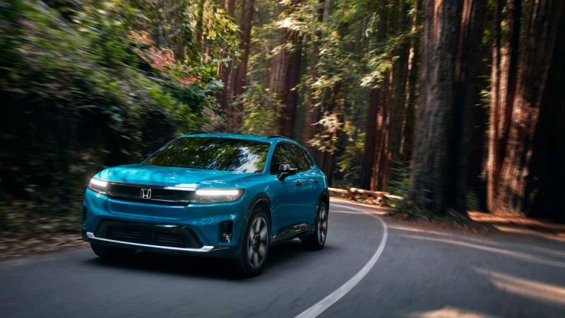 A light blue Honda Prologue travels down windy, wooded road