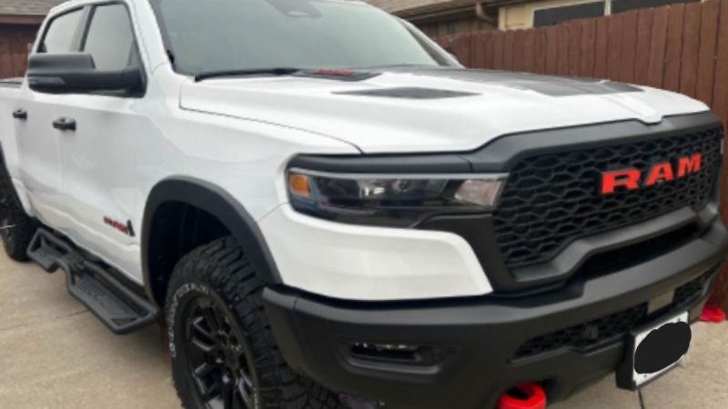 White Ram 1500 pickup truck shown from a front three-quarter angle, featuring its distinctive black mesh grille with red Ram lettering and aggressive off-road bumper design.