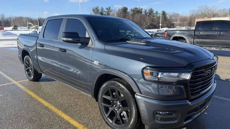 James' gray/charcoal 2026 Ram 1500 pickup truck shown from the front three-quarter angle, featuring black wheels and a blacked-out grille in a parking lot setting.