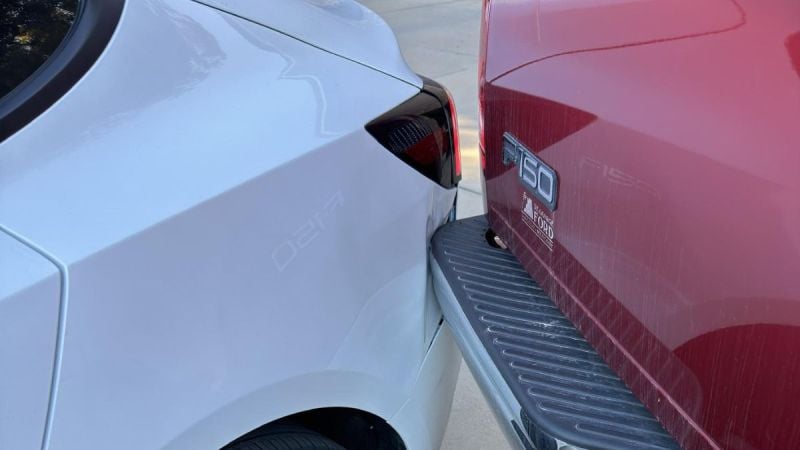 Close-up detail shot of a Ford F-150 truck's rear being dented in by a 2025 Tesla Model 3.