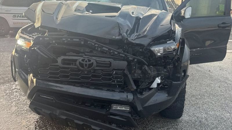 Jerry's Toyota Tacoma with severe front-end collision damage, showing a damaged grille, bumper, and hood from a front three-quarter view.