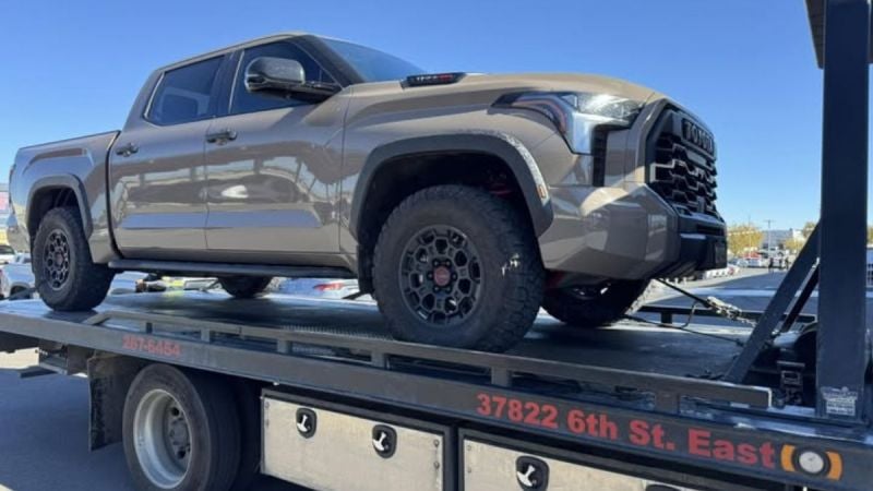A tan 2025 Toyota Tundra with rugged tires is secured on a flatbed tow truck under a clear blue sky. The scene conveys a sense of utility and readiness.