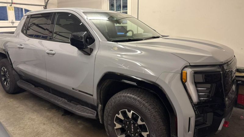 A grey GMC Sierra EV parked in a garage. The truck has large tires and tinted windows, conveying a rugged yet modern design.